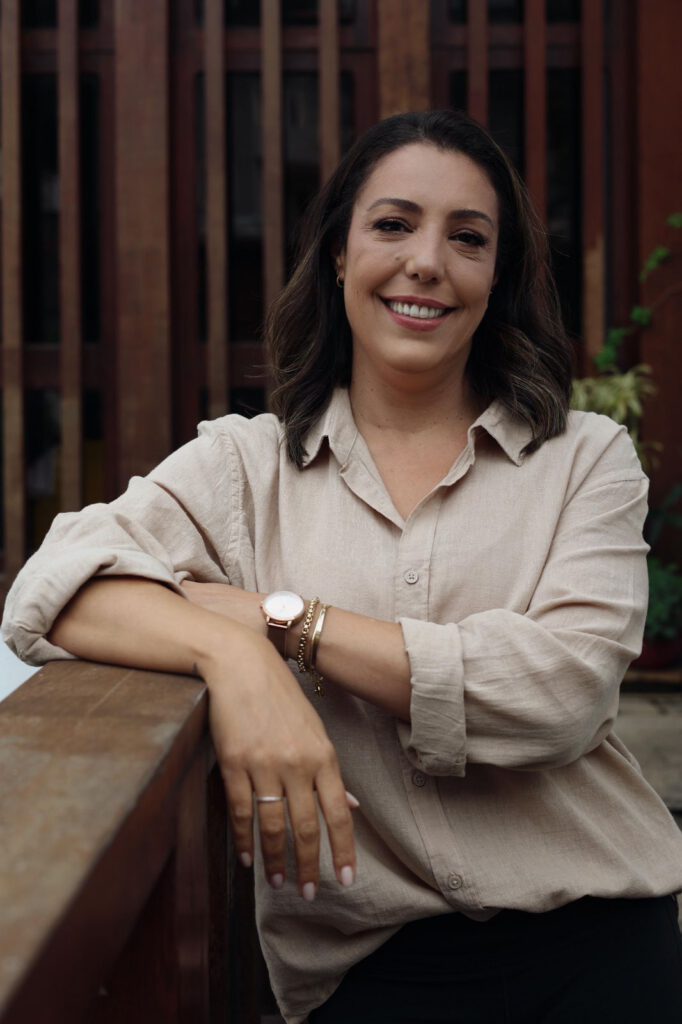 Ana Paula Alves Rodrigues, sorrindo, apoiada em um parapeito de madeira